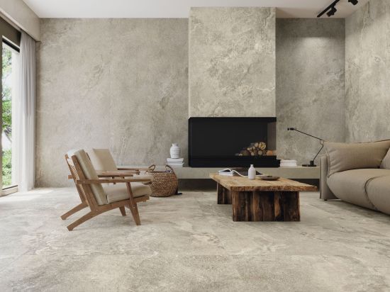 Minimalistyczny salon wyłożony beżowymi płytkami imitującymi kamień Dome Nut z kominkiem, kanapą, dwoma fotelami i drewnianym stołem