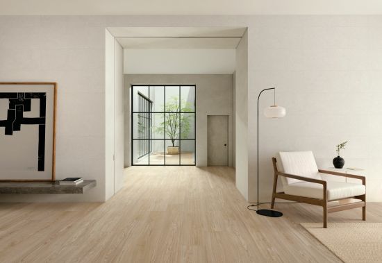 Przestronne, minimalistyczne pomieszczenie z jasną podłogą wyłożoną płytkami drewnopodobnymi Granier Maple, z fotelem i lampą stojącą oraz wiszącą p&oacute;łką z obrazem