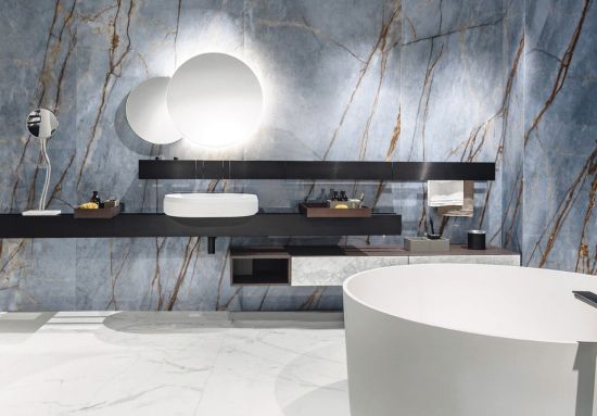 Luksusowa łazienka z niebieskimi płytkami Florim Heritage Luxe Azure o wzorze marmuru. Widoczna biała wanna wolnostojąca, nowoczesna umywalka i okrągłe, podświetlane lustra.