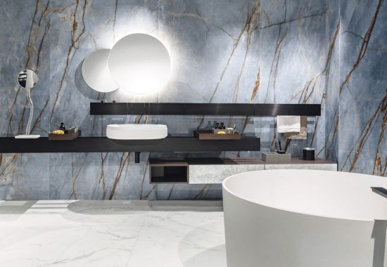 Wizualizacja luksusowej łazienki ze ścianą z niebieskiego marmuru Florim Heritage Luxe Azure. Wnętrze posiada białą nablatową umywalkę, okrągłe podświetlane lustra i wolnostojącą matową wannę.