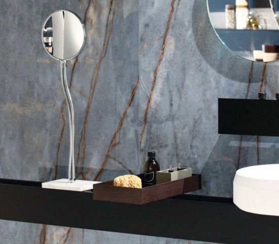 Detale nowoczesnej łazienki ze ścianą z niebieskiego marmuru Florim Heritage Luxe Azure. Na czarnym blacie stoi biała umywalka, drewniana taca z kosmetykami oraz okrągłe lusterko kosmetyczne.