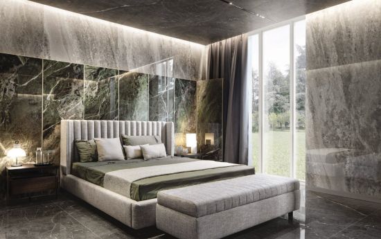 Elegancka sypialnia ze ścianami z zielonego marmuru Florim Heritage Luxe Emerald i szarych spiek&oacute;w Cloud. Na środku stoi tapicerowane ł&oacute;żko z pionowo przeszywanym zagł&oacute;wkiem i dopasowaną ławą.