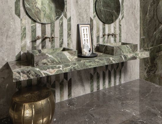 Elegancki salon: duża szara sofa, ciemna podłoga z żyłowaniem i dekoracyjna ściana z płyt wielkoformatowych imitujących marmur w odcieniach brązu i beżu. Minimalistyczny stolik kawowy w centrum.
