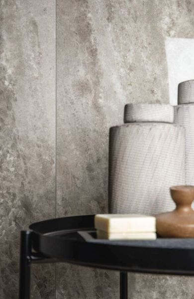 Zbliżenie na szare, wielkoformatowe płyty Florim Heritage Cloud imitujące kamień. Na pierwszym planie czarny stolik z mydłem i ceramicznymi akcesoriami łazienkowymi w stonowanych kolorach.