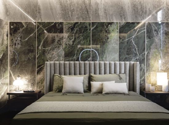 Elegancka sypialnia: tapicerowane ł&oacute;żko na tle dekoracyjnej ściany ze spiek&oacute;w kwarcowych Florim Heritage Luxe Emerald i Cloud. Widoczne stoliki nocne z zapalonymi lampkami.