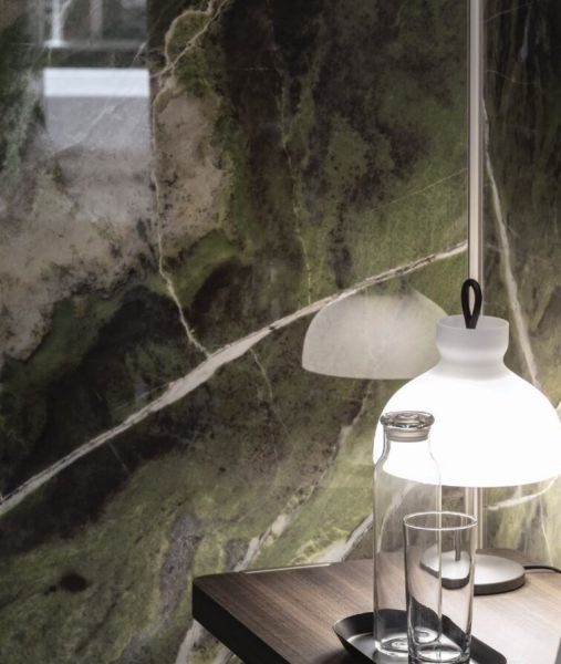 Zbliżenie na zielone, wielkoformatowe płyty Florim Heritage Luxe Emerald o wzorze marmuru. Obok biała lampa stołowa Arenzano, szklana karafka i szklanka na ciemnym, drewnianym blacie.