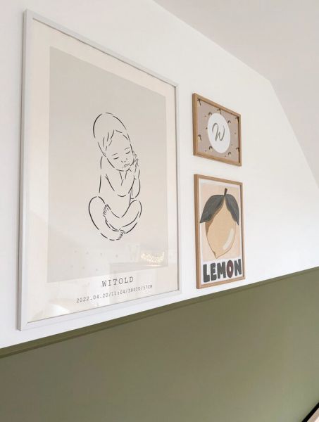 Galeria trzech plakat&oacute;w na białej ścianie nad zieloną lamperią. Największy z nich, w jasnej ramie, przedstawia liniowy szkic niemowlęcia z metryczką. Obok wiszą dwa mniejsze obrazki w drewnianych ramkach: litera W oraz ilustracja cytryny.
