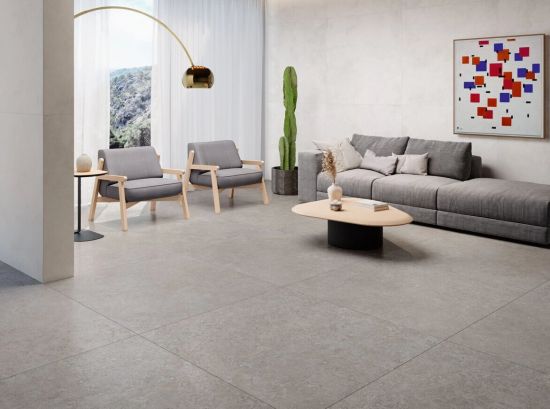 Nowoczesny salon z szarymi, wielkoformatowymi płytkami gresowymi. Wnętrze zdobią dwa szare fotele, duża kanapa, designerska lampa oraz abstrakcyjny obraz z kolorowymi kwadratami.