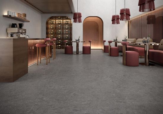 Wnętrze nowoczesnej restauracji z ciemnoszarą, nakrapianą podłogą. Po lewej stronie drewniany bar z hokerami i ekspresem. Po prawej stoliki z bordowymi pufami i kanapami na tle drewnianych lamel. W tle wysokie łuki, regał na wino i wiszące lampy.