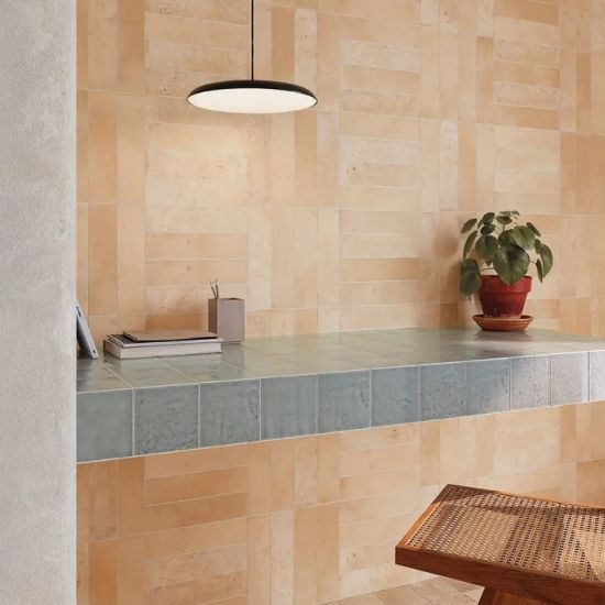 Nowoczesne wnętrze z beżowymi płytkami na ścianie, niebiesko-szarym blatem z kafelk&oacute;w, drewnianym stołkiem i rośliną.