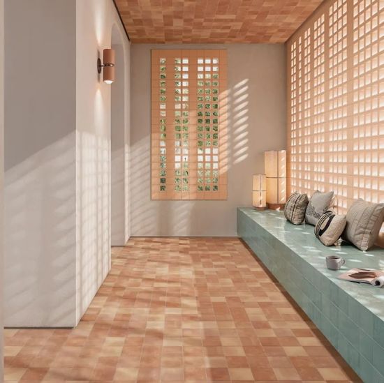 Nowoczesne wnętrze z podłogą z terakotowych i beżowych kwadratowych płytek, miętową ławką z poduszkami i sufitem wyłożonym terakotą.