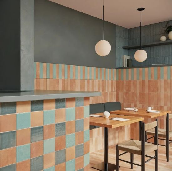 Nowoczesne wnętrze restauracji z kafelkami w kolorach terakoty i mięty, drewnianymi stołami i lampami wiszącymi.