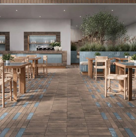Wnętrze restauracji lub kawiarni z podłogą wyłożoną brązowymi i niebieskimi płytkami drewnianymi stołami i krzesłami barem z niebieskimi kaflami i dużą rośliną doniczkową w głębi.