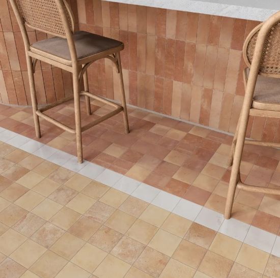 Nowoczesne wnętrze baru z podłogą i ścianą wyłożoną terakotowymi i beżowymi płytkami, oraz dwoma wiklinowymi hokerami.
